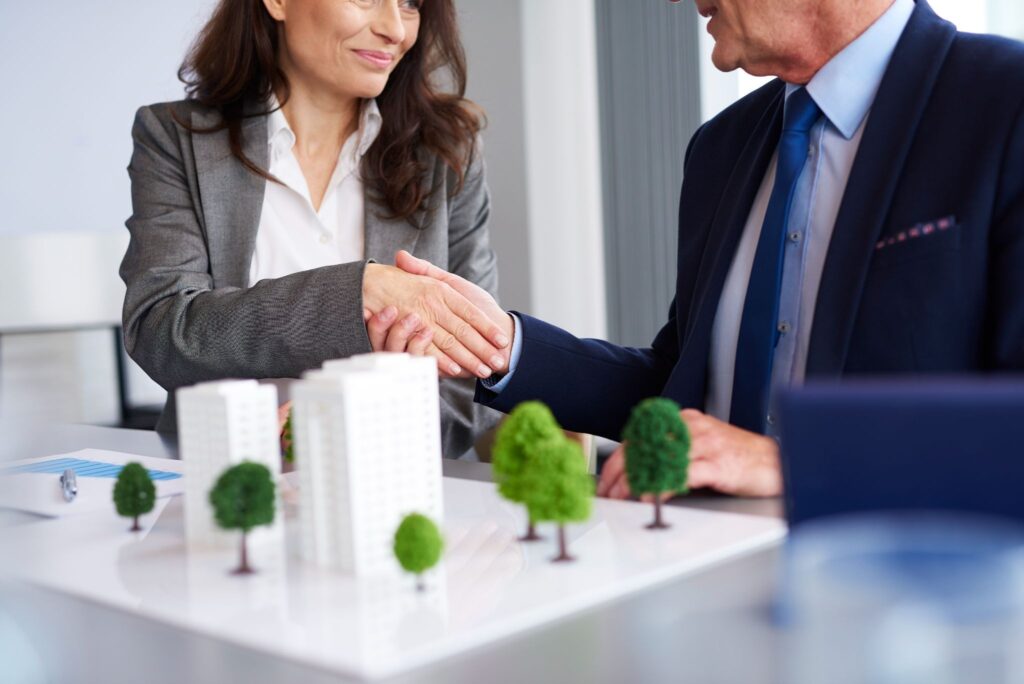 A businesswoman and businessman shaking hands across a desk.