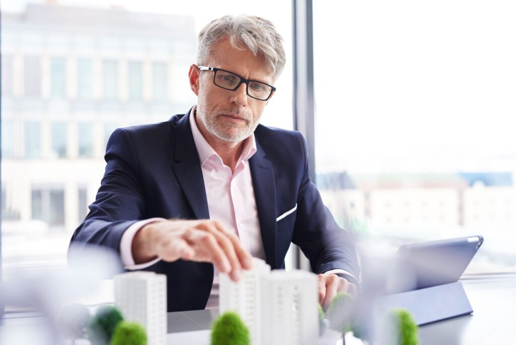 Mature businessman in a suit examining a scale model of a residential building development.