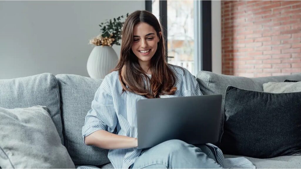 Smiling woman reviews trust options on laptop, weighing control versus asset protection from her living room couch.