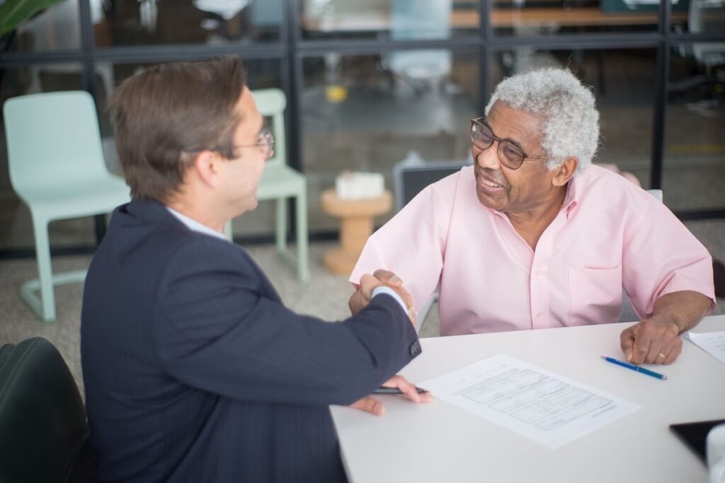 Two men shake hands over documents after a nonprofit compliance consultation.
